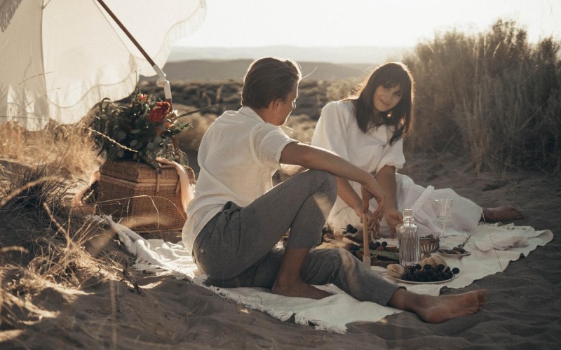 a man and woman sitting on a beach with an umbrella